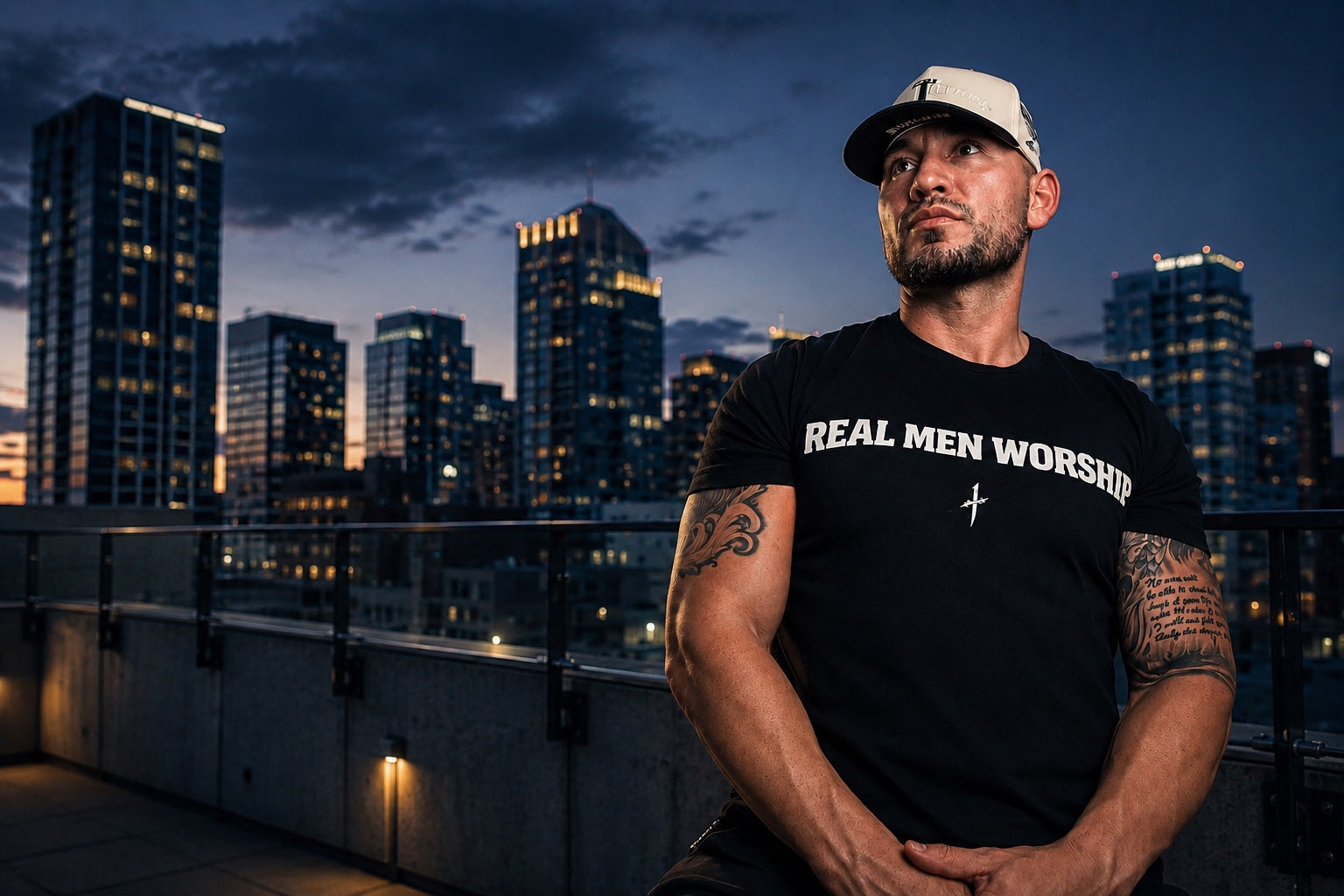 Man wearing the King of Kings snapback and a black Real Men Worship shirt on a city rooftop